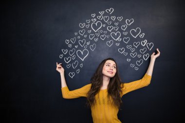 Happy woman posing over black board with drawn hearts 
