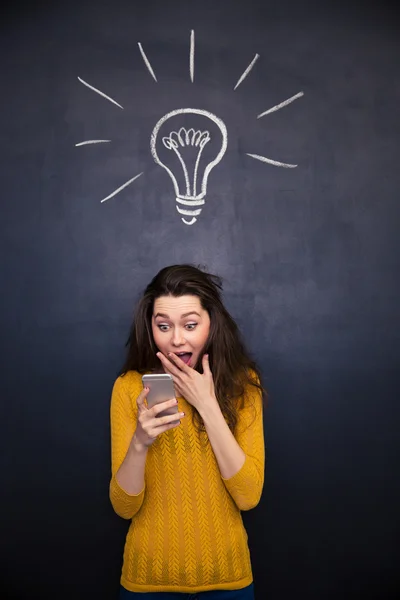Удивительная счастливая женщина использует мобильный телефон на фоне доски — стоковое фото