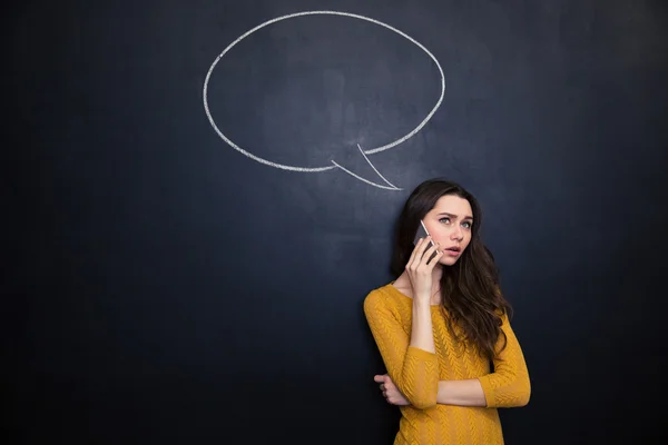 Thoughtful female talking on mobile phone over blackboard background — Stok fotoğraf