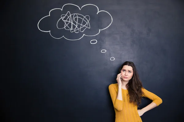 Unhappy woman talking on cellphone standing over background of chalkboard — Stock Photo, Image