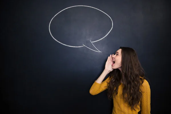 Charming woman screaming against background of chalkboard with speech bubble — Stock fotografie