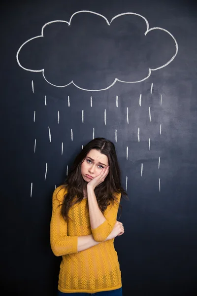 Mulher triste em pé sob a nuvem de chuva desenhada acima dela no quadro negro — Fotografia de Stock