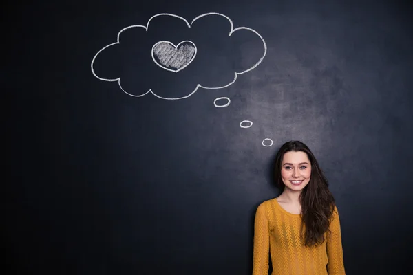 Woman thinking about love and standing with blackboard behind her — Zdjęcie stockowe