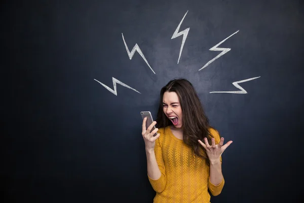 Crazy woman using smartphone and yelling over blackboard — Stock fotografie