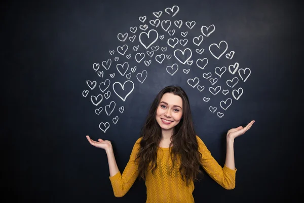 Beautiful woman holding drawing hearts on palms over blackboard — Stock Photo, Image