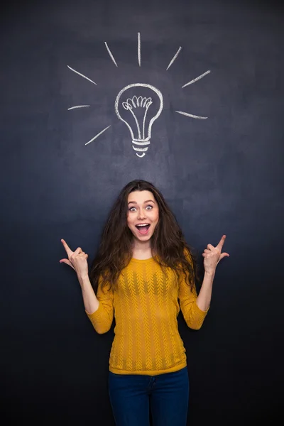 Happy surprised woman ponting up over chalkboard background — Stock Fotó