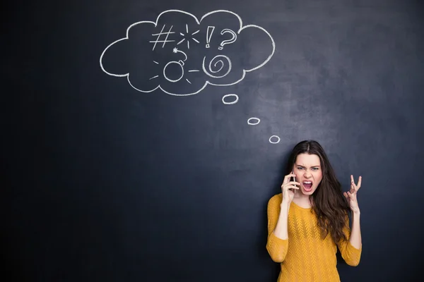 Crazy woman screaming on mobile phone standing over chalkboard background — Zdjęcie stockowe