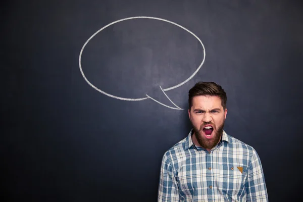 Angry man shouting over blackboard background with drawn speech bubble — Stock Photo, Image