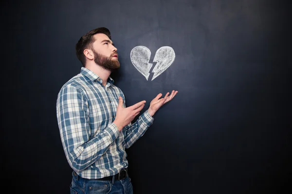 Trauriger romantischer Mann hält gezeichnetes gebrochenes Herz über Tafel-Hintergrund — Stockfoto