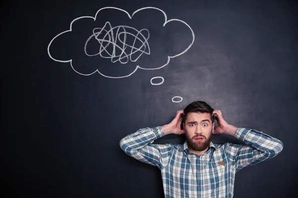Confused man thinking about problem with black board behind him — Stock Photo, Image