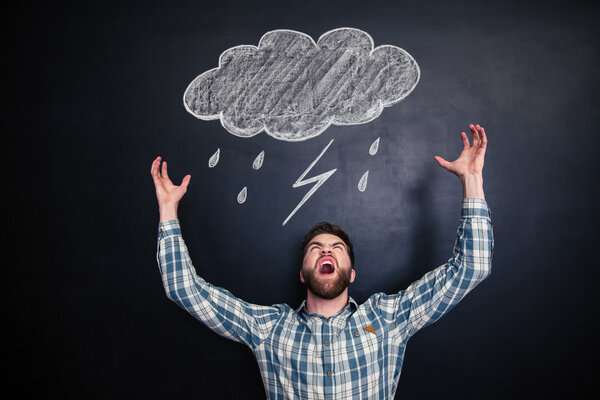 Angry man standing and shouting over blackboard with drawn raincloud