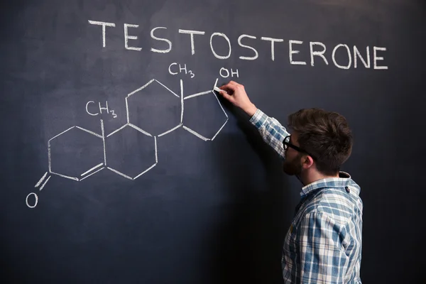 Estudante concentrado desenhando estrutura química da molécula de testosterona no quadro negro — Fotografia de Stock