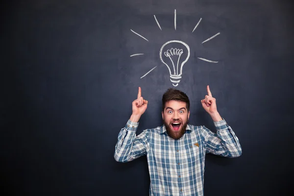 Surprised man pointing up with both hands over chalkboard background — Stock Photo, Image