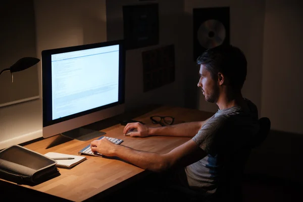 Uomo seduto in camera oscura e utilizzando il computer — Foto Stock