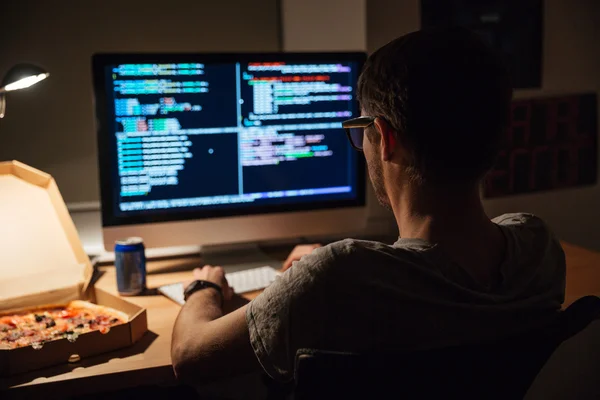 Visão traseira do programador focado escrevendo código e comendo pizza — Fotografia de Stock