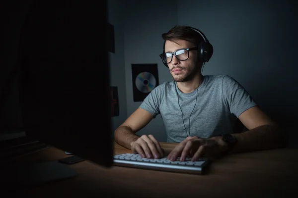 Konzentrierter junger Mann mit Kopfhörern am Computer — Stockfoto