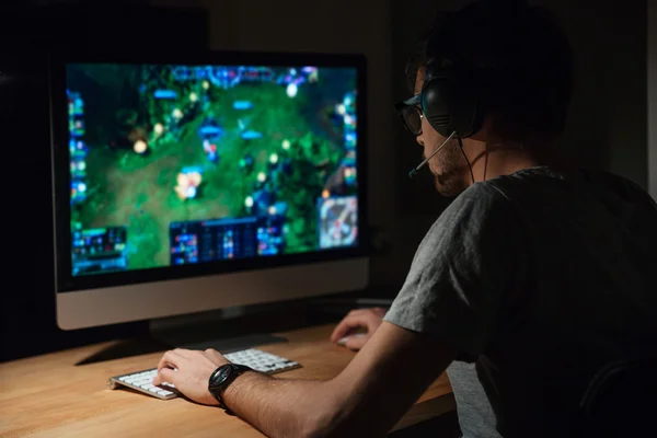 Concentrated gamer in headphones using computer for playing game — Stock Photo, Image