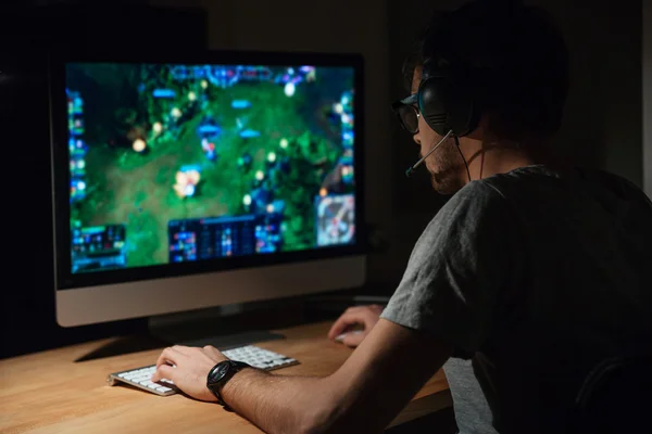 Konsentrat gamer dalam headphone menggunakan komputer untuk bermain game Stok Foto