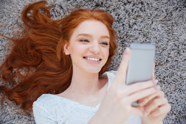 Vrouw liggend op het tapijt en het gebruik van smartphone — Stockfoto