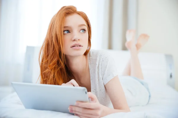 Nachdenkliche Frau liegt mit Tablet-Computer im Bett — Stockfoto