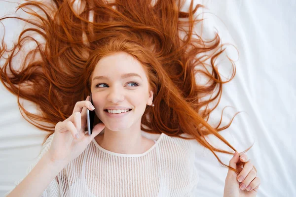 Веселая игривая женщина разговаривает по мобильному телефону в постели — стоковое фото