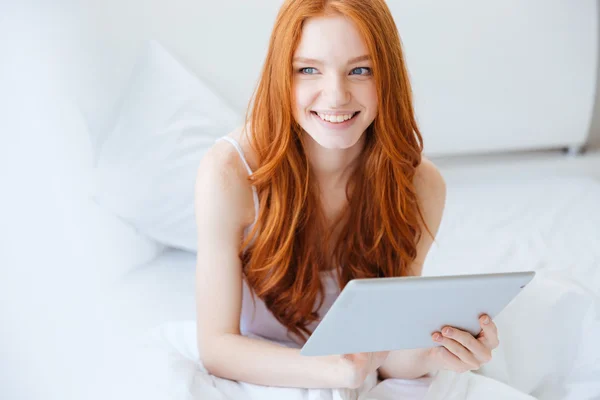 Cheerful woman sitting on bed and using laptop — Stock Photo, Image