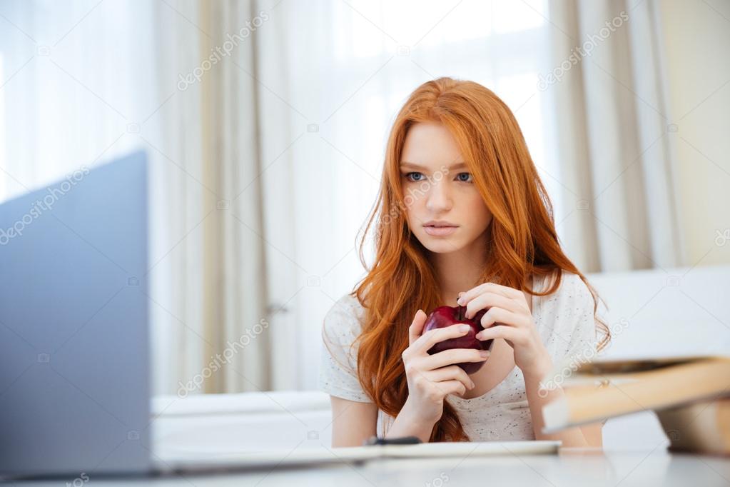 Woman holding apple and looking on laptop computer screen 