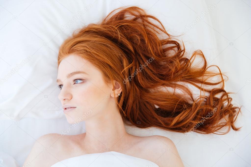 Attractive woman with beautiful long red hair lying in bed
