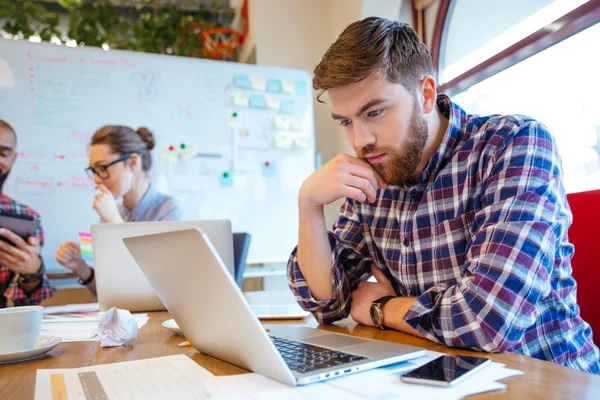 Concentrated man using laptop while his friends studying together — Stock Photo, Image