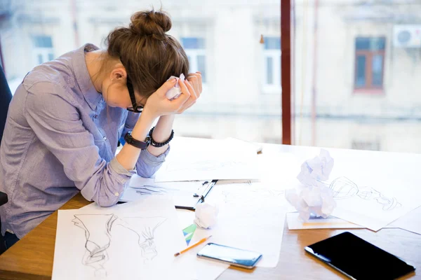 Verzweifelte Modedesignerin sitzt mit Skizzen im Büro — Stockfoto