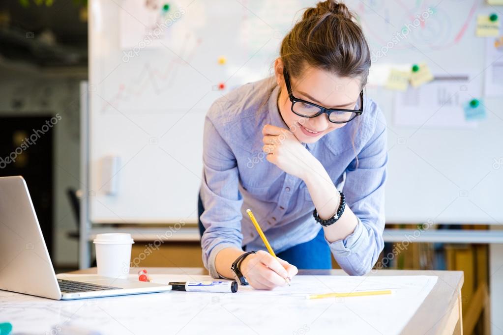 Pretty young woman drawing blueprint by pencil in the office