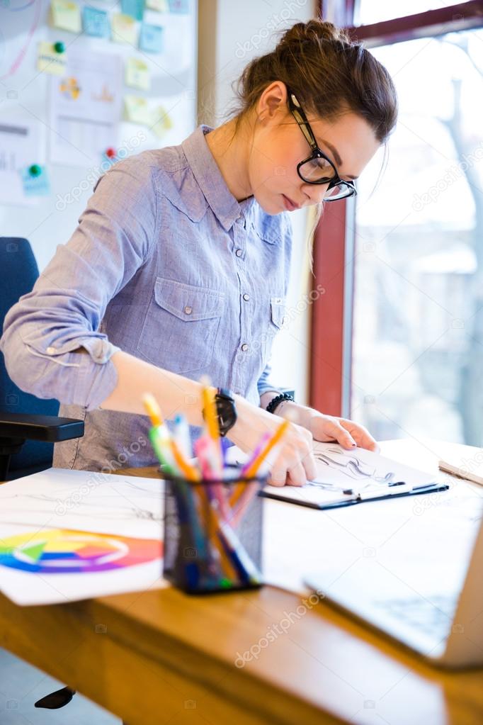 Focused woman fashion designer drawing sketches on workplace