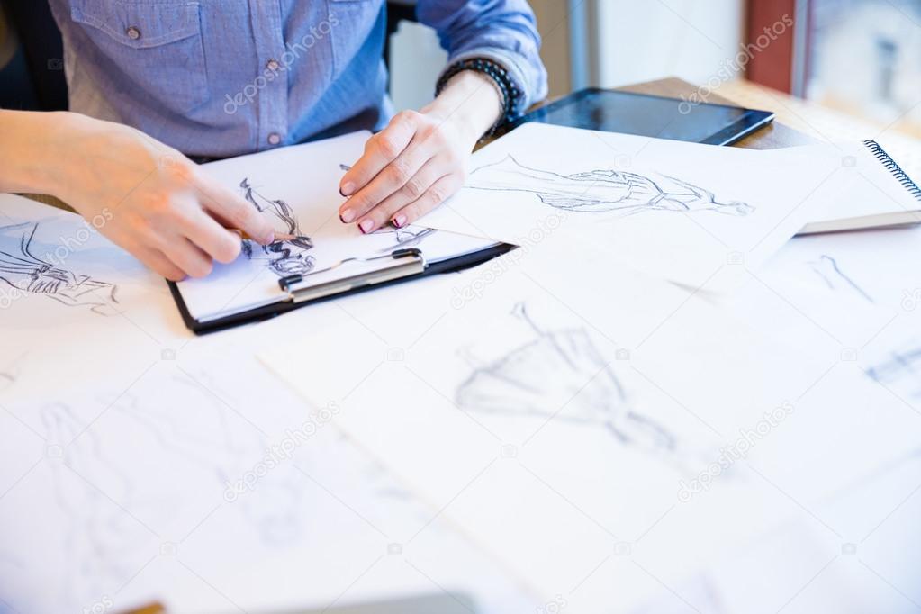 Fashion designer creating new clothes and drawing sketches on clipboard