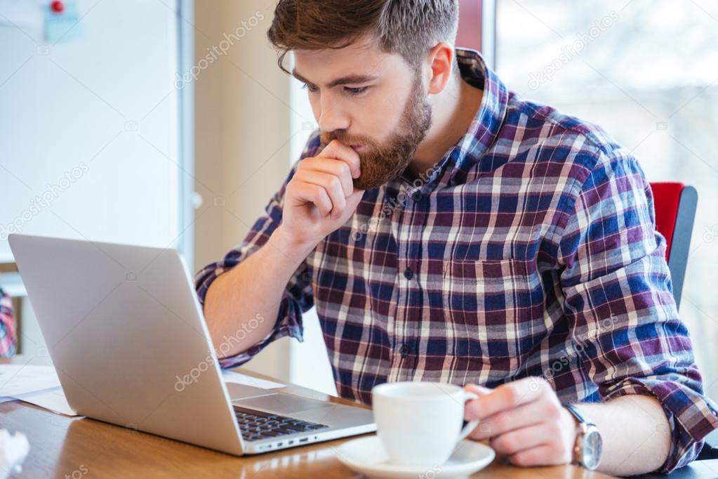 Serious focused man sitting at the table and using laptop