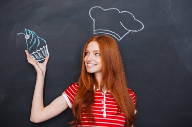 Woman in drawn chef hat holding drawing cupcake over blackboard 