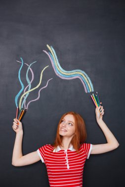 Happy woman holding colorful pencils and drawing on chalkboard background