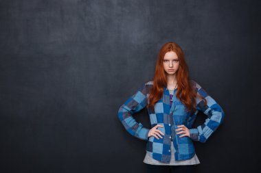 Serious woman standing with hands on waist over blackboard background