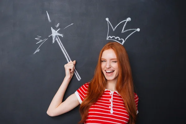 Cute woman winking with crown and magic wand over chalkboard — Stock Photo, Image