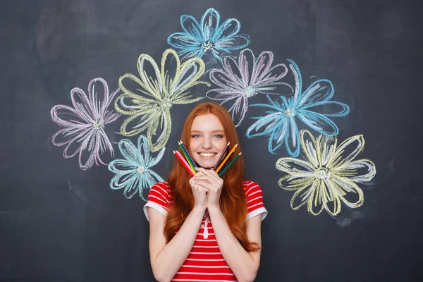 Gelukkige vrouw met potloden over schoolbord achtergrond met getekende bloemen — Stockfoto