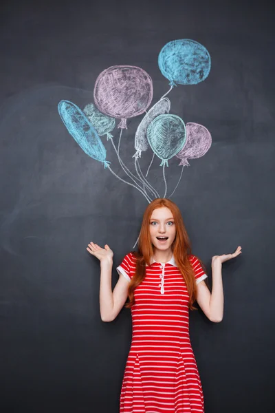 Surprised excited woman standing over chalkboard background with drawn balloons — Stockfoto