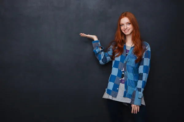 Smiling woman holding copyspace on palm over blackboard background — Stock Fotó