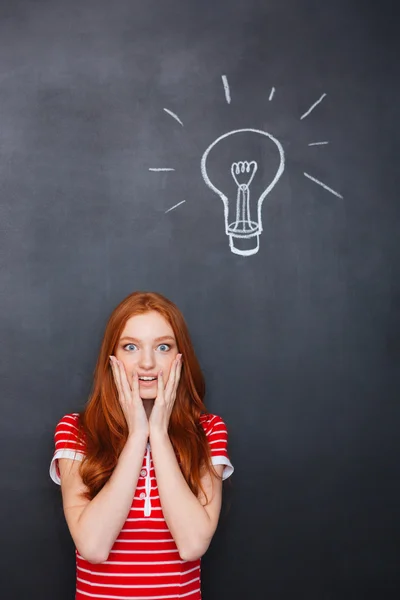 Amazed woman standing over chalkboard background with drawn electric bulb — Stok fotoğraf