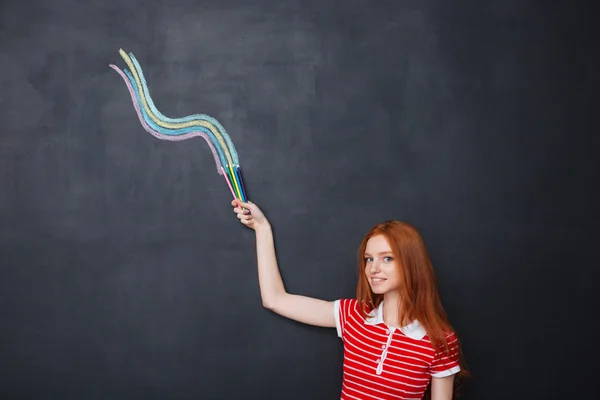 Smiling woman drawing wave with colorful pencils on blackboard background — Stock fotografie