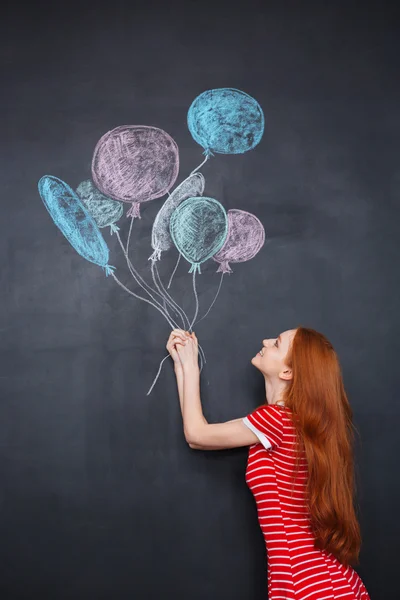 Cute woman holding colorful balloons drawn on chalkboard background — Stockfoto
