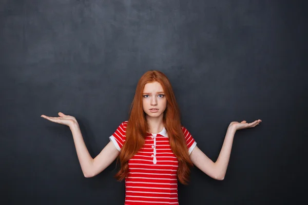 Verwirrte Frau hält Kopierraum auf beiden Handflächen über Tafelhintergrund — Stockfoto