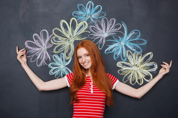 Cheerful woman standing over blackboard with drawn colorful flowers — ストック写真