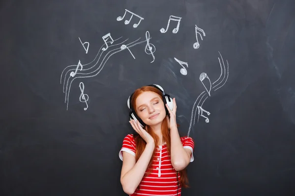 Relaxed woman listening to music in headphones over chalkboard background — 图库照片