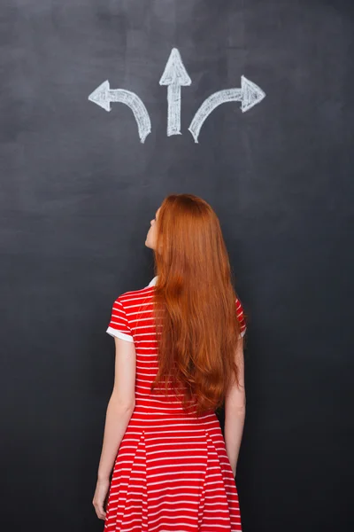 Back view of woman choosing direction over chalkboard background — Zdjęcie stockowe