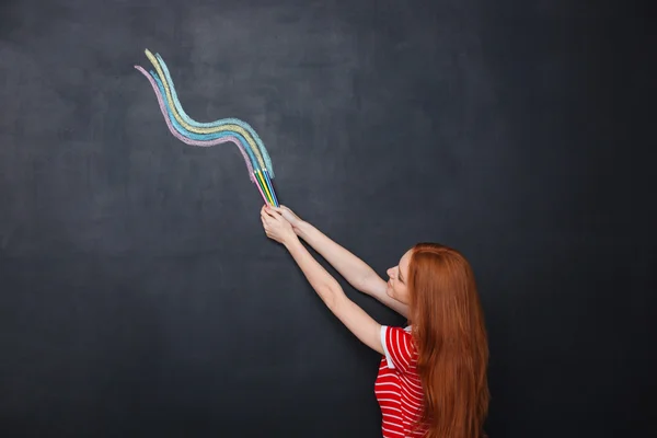 Beautiful woman drawing colorful wave on chalkboard background using pencils — Stock fotografie