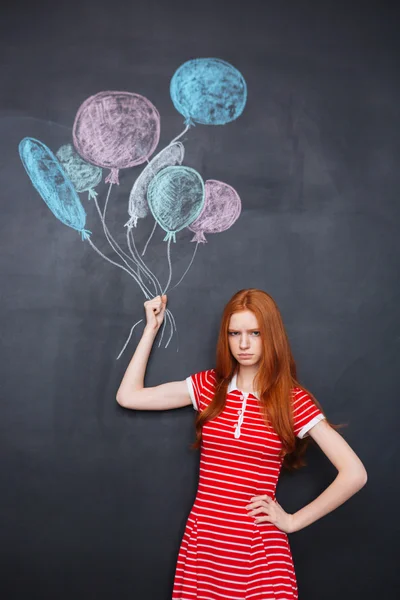 Sad girl holding drawn colorful balloons over blackboard background — Zdjęcie stockowe